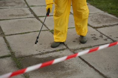 Person in hazmat suit disinfecting street pavement with sprayer, closeup. Surface treatment during coronavirus pandemic