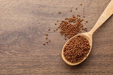 Photo of Spoon with buckwheat tea granules on wooden table, top view. Space for text