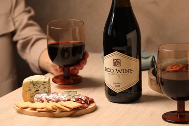 Woman holding glass of red wine at table with different snacks, closeup