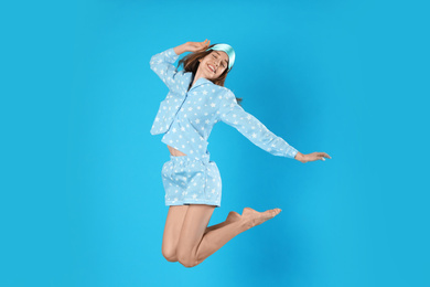 Beautiful woman with sleep mask jumping on light blue background. Bedtime