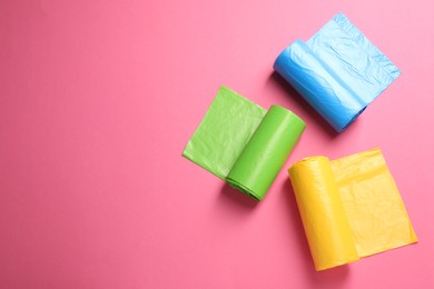 Photo of Rolls of different garbage bags on pink background, flat lay. Space for text
