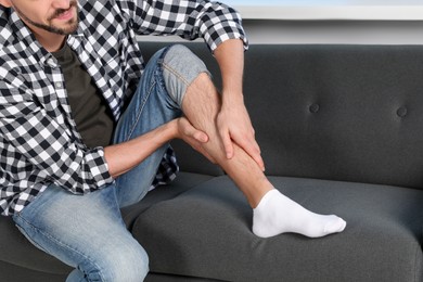 Man rubbing sore leg on sofa at home
