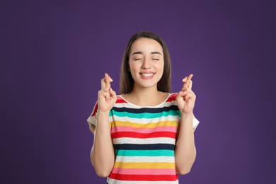 Woman with crossed fingers on purple background. Superstition concept