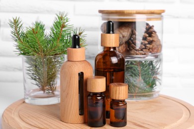 Photo of Bottles of essential oil, pine branches and cones on wooden board