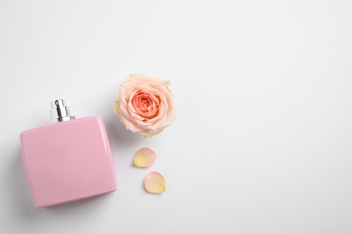 Bottle of perfume, beautiful rose and petals on white background, flat lay