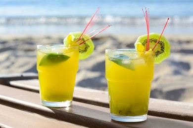 Glasses of refreshing drink with kiwi and mint on wooden bench near sea