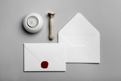 Envelopes with wax seal, candle and stamp on grey background, flat lay