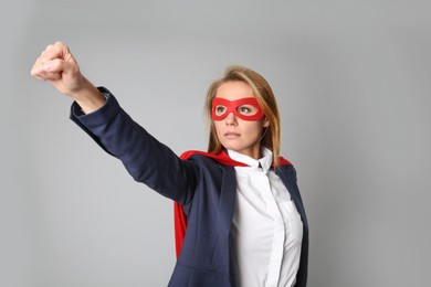 Confident businesswoman wearing superhero cape and mask on light grey background