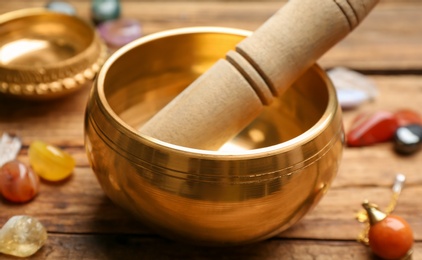 Golden singing bowl with mallet on wooden table, closeup. Sound healing
