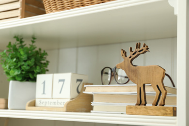 White shelving unit with wooden deer figure, books and calendar