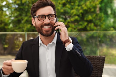 Handsome bearded man with cup of coffee talking on phone in outdoor cafe