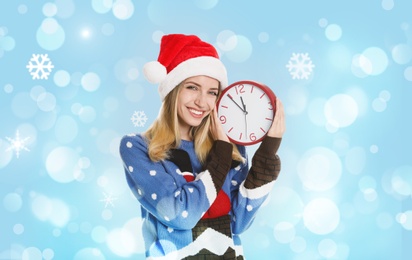 New Year countdown. Happy woman in Santa hat holding clock on light blue background