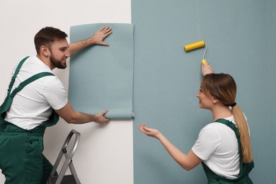 Workers hanging stylish wall paper sheet on light background