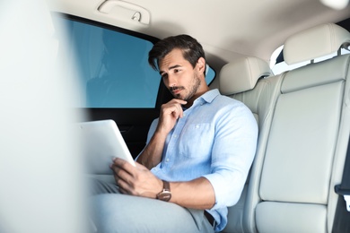 Photo of Thoughtful young man with tablet on backseat in luxury car