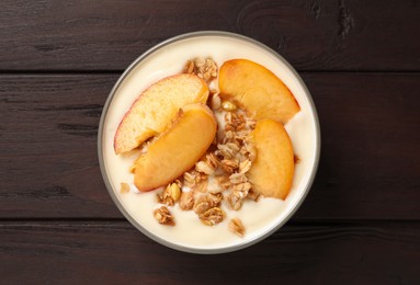 Tasty peach yogurt with granola and pieces of fruits in bowl on wooden table, top view
