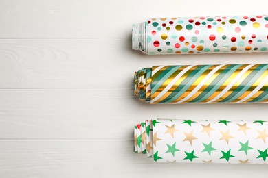 Different colorful wrapping paper rolls on white wooden table, flat lay. Space for text