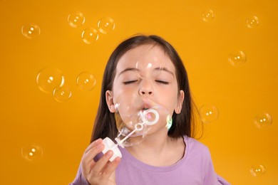 Little girl blowing soap bubbles on yellow background