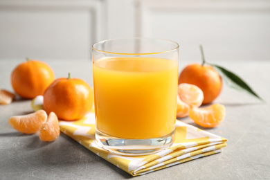 Glass of fresh tangerine juice and fruits on light grey table