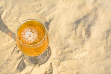 Photo of Glass of cold beer on sandy beach, above view. Space for text