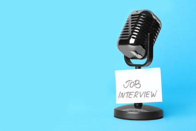 Retro microphone and reminder note with words JOB INTERVIEW on light blue background, space for text