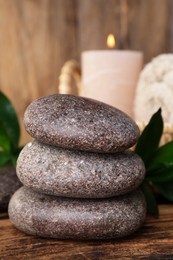 Stacked spa stones, bamboo leaves and candle on wooden table, closeup