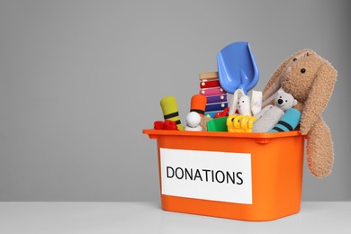 Donation box with different toys on white table against grey background. Space for text
