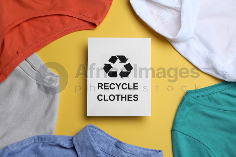 Photo of Different clothes with recycling label on yellow background, flat lay