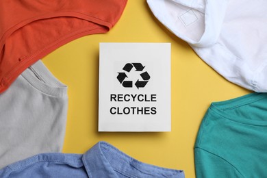 Photo of Different clothes with recycling label on yellow background, flat lay