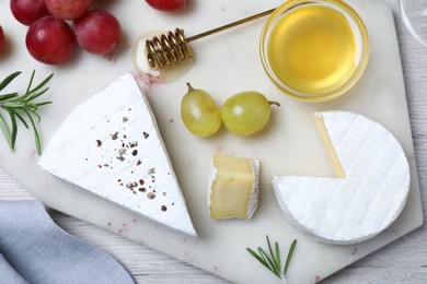 Tasty brie cheese with honey, rosemary and grapes on white board, flat lay