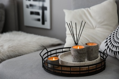 Candles and aroma reed diffuser on grey sofa, space for text