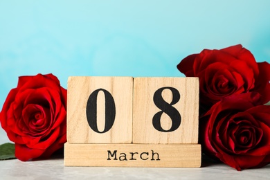 Wooden block calendar with date 8th of March and roses on table against light blue background. International Women's Day