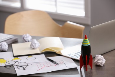 Toy rocket, laptop and stationery on messy table in office, space for text. Startup concept