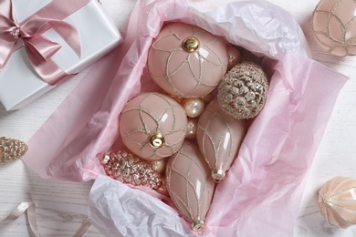 Collection of beautiful Christmas tree baubles and gift box on white wooden table, flat lay