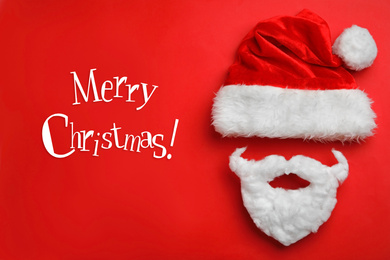 Text MERRY CHRISTMAS and Santa Claus hat with beard on red background, flat lay