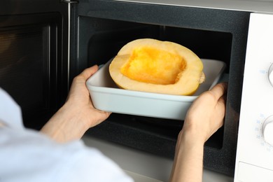 Photo of Woman putting half of fresh spaghetti squash into microwave oven, closeup