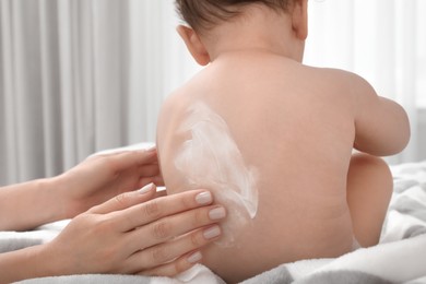 Mother applying body cream on her baby indoors, closeup