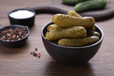 Bowl of pickled cucumbers and ingredients on wooden table, closeup