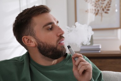 Handsome young man using disposable electronic cigarette at home
