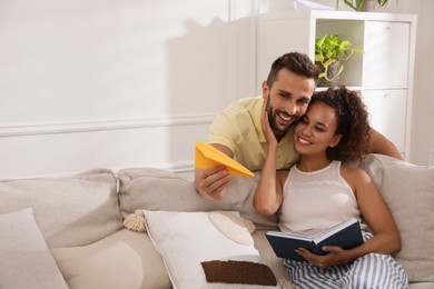 Happy man playing with paper plane while his girlfriend reading book on sofa in living room