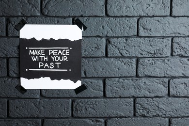 Photo of Card with life-affirming phrase Make Peace With Your Past on dark brick wall. Space for text
