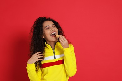 African American woman eating French fries on red background, space for text