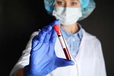 Scientist holding test tube with blood sample and label CORONA VIRUS against black background, focus on hand