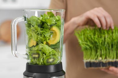 Photo of Man holding microgreen peas for delicious smoothie and blender with ingredients indoors, closeup