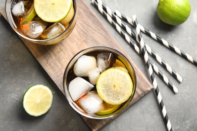 Glasses of cocktail with cola, ice and cut lime on grey background, flat lay
