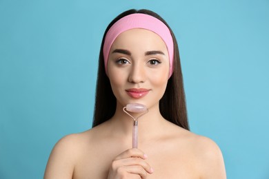 Woman using natural face pink quartz roller on light blue background