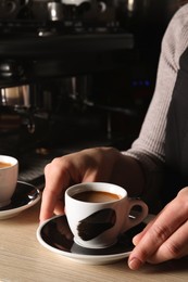 Barista with cup of fresh aromatic coffee at wooden counter in cafe, closeup