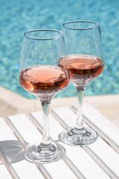 Photo of Glasses of tasty rose wine on white wooden table near swimming pool, closeup