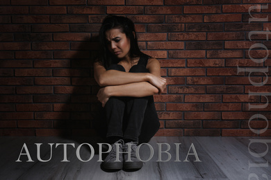 Depressed young woman sitting alone near brick wall. Autophobia - fear of isolation