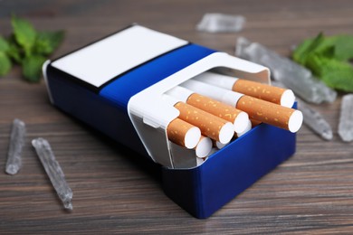Pack of cigarettes and menthol crystals on wooden table, closeup