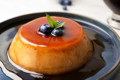 Photo of Plate of delicious caramel pudding with blueberries and mint on table, closeup